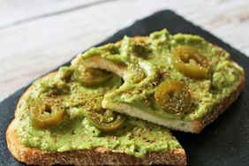 halved toast with guacamole, jalapeno slices, and crushed pepper on black board