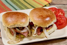 two fried bologna and onion sliders on a white plate with tomato slices