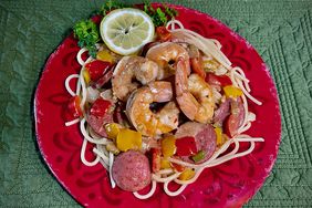 Cajun shrimp, sausage and bell peppers over spaghetti on red plate