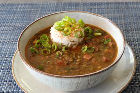 white bowl of lentil soup with scoop of white rice and green onion garnish on blue placemat