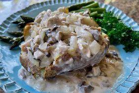 baked potato with a chicken cream and mushroom sauce on blue plate with asparagus in background