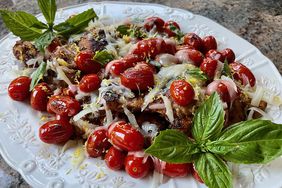 white platter with chicken thighs covered in blistered tomatoes, mozzarella and basil