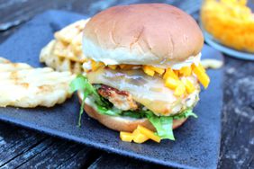 beautifully grilled chicken burger with melted cheese, lettuce, and mango, on square blue ceramic plate