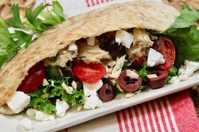 pita sandwich with tuna, tomatoes, lettuce, olives, on white plate with red and white napkin