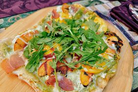 homemade pizza on wooden board topped woth prosciutto, grilled peaches, and arugula