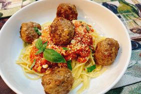 white bowl of browned meatballs on bed of spaghetti and sauce