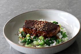 slice of meatloaf on bed of bok choy rice with dark sauce and sesame seeds in ceramic bowl