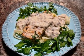 light blue fluted ceramic plate with fettucine, browned chicken cutlet, and creamy mushroom sauce, garnished with parsley