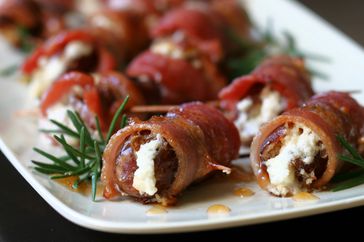 closeup of bacon wrapped, goat cheese-stuffed dates on white platter with rosemary sprigs
