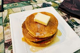 stack of pumpkin pancakes on white plate with syrup and a pat of cold butter