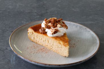 beautiful wedge of butternut squash cheesecake with whipped cream and candied walnuts on soft gray plate