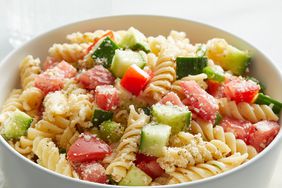 mid angle looking at a large bowl full of pasta salad with cucumbers, tomatoes, pasta and cheese 
