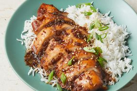 high angle, looking down at a place of white rice, topped with sliced bourbon chicken, and garnished with thinly sliced green onions.