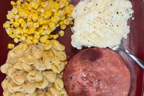 close up view of baked ham steak with pasta, corn and mashed potatoes