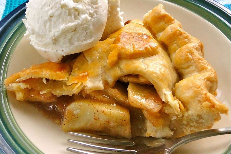 a slice of double-crust apple pie garnished with an apple-shaped pastry cutout and a scoop of vanilla ice cream