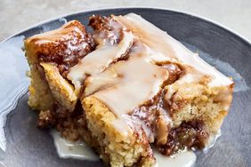 slice of Cinnabon cinnamon roll cake with icing drizzled on top on a gray plate.