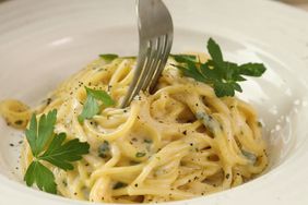 a bowl of spaghetti topped with chopped parsley, with a fork twirling a bite