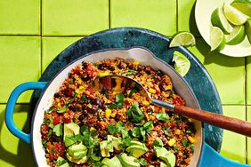 Black beans, tomatoes, and quinoa topped with avocado and fresh herbs in a turquoise skillet
